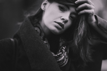 Attractive charming young woman in a dark coat walking in the autumn park. Cloudy. Soft colors of nature. The melancholy mood. Black and white photo. Film grain.
