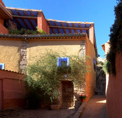 A sloped street in the typical Spanish town Anento, with a stone and bricks house, a climbing rose...
