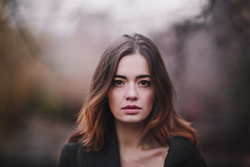 Attractive charming young woman in a dark coat walking in the autumn park. Cloudy. Soft colors of nature. The melancholy mood.