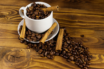 Coffee beans in white cup and cinnamon sticks on wooden table