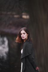 Attractive charming young woman in a white cotton dress and dark coat walking in the autumn park. Cloudy. Soft colors of nature. The melancholy mood.