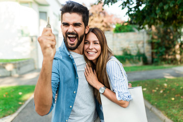 Happy young couple with key  in hand standing outside in front of their new home. - obrazy, fototapety, plakaty
