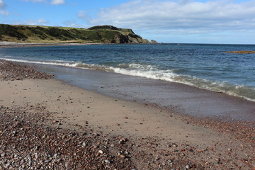 Waves arriving on sandy beach with pebbles and cliffs in background