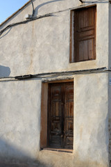 A restored two sided brown door in a white and beige wall with some cables passing over it in the Almonacid de la Cuba rural country town in Aragon Region, Spain, at sunset