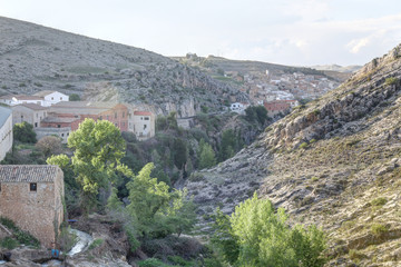 A landscape at the sunset of the rural town of Almonacid de la Cuba, in Spain, with houses on a small valley with the Aguavivas river and waterfall. An ancient Roman bridge is crossing the river.