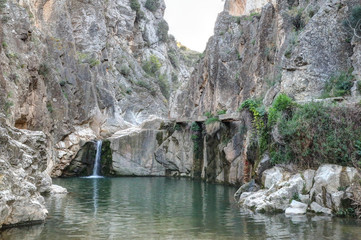 A rural landscape of a small lake and Aguavivas river waterfalls inside a rocky canyon dug by the warer, at the sunset, in the Aragon region, Spain