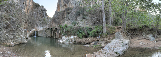 A rural landscape of a small lake and Aguavivas river waterfalls inside a rocky canyon dug by the warer, and a stone bridge, at the sunset, in the Aragon region, Spain
