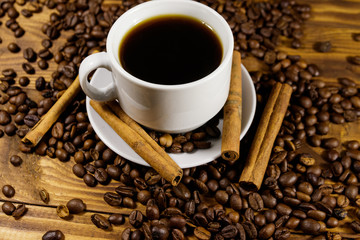 Cup of coffee, roasted coffee beans and cinnamon sticks on wooden table