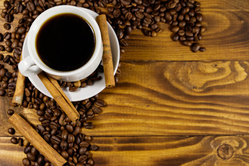 Cup of coffee, roasted coffee beans and cinnamon sticks on wooden table. Top view, copy space
