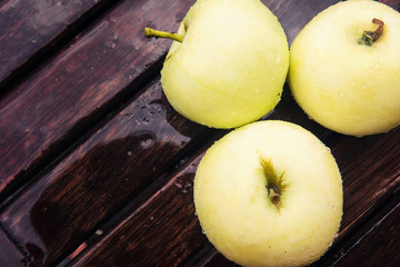 Three yellow apples on dark wood