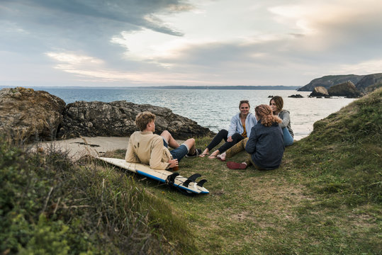 Happy friends with surfboard socializing at the coast at sunset