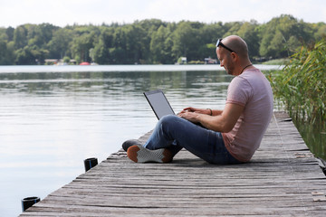 41-year-old athletic man works in Brandenburg near a lake with smartphone and laptop.
