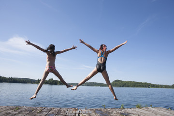 Twin girls jumping off dock.