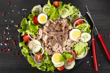 Salad with tuna, anchovies and vegetables. Mediterranean food. The background is black. Top view. Copy space. Horizontal shot.