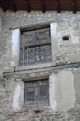 Fototapeta premium Two smal windows with old shabby wooden shutters and a railing on a stone grey houes in Biel, a small town in Aragon, Spain