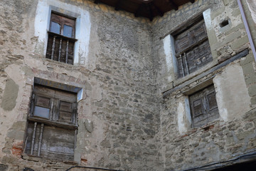 Fototapeta na wymiar Four smal windows with old shabby wooden shutters and a railing on a stone grey houes in Biel, a small town in Aragon, Spain