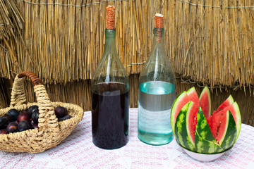 Bottles of wine and moonshine on the table. A basket with a plum and a watermelon as a snack. Traditional alcoholic drinks.