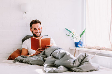 Fototapeta premium Young man reading a book in the bed