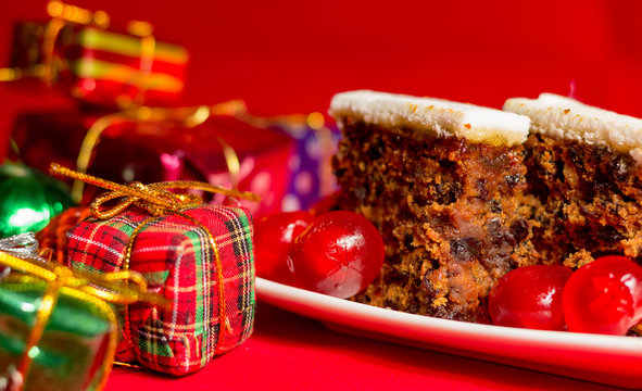 Fruitcake and small gifts depicting Christmas celebrations on red background