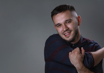 Friendly young man smiling in to the camera. Half side portrait handsome in checkered and cross hands. Copy space grey background