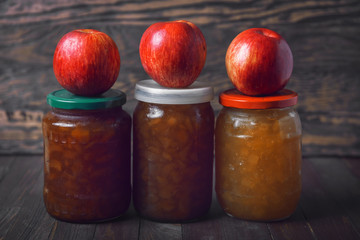 Jars with jam and red apples on a wooden background
