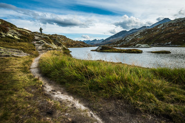 Fototapeta na wymiar man walking in a mountains trail in switzerland alps with lake and cloudy sky
