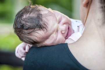 Sweet hungry newborn baby girl crying desperately on a shoulder of her mother. Stomach cramps, baby...