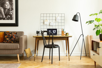Black, wooden chair and an industrial floor lamp by a vintage desk with a laptop in a white living room interior