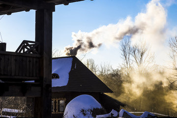 wooden house with a submerged stove and smoke leaving in the sky on a sunny winter day