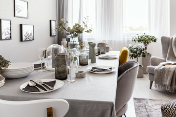 Close-up of a well-laid table with plates and glasses in a grey dining room interior. Real photo