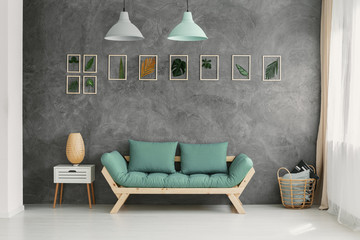 Wooden sofa with mint green cushions by a gray wall with a botanic gallery in a scandinavian living room interior