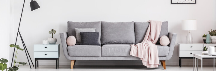 Fototapeta na wymiar Grey lounge with cushions and pastel pink blanket in real photo of white living room interior