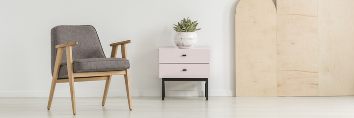 Grey retro armchair standing in real photo of white room interior with pastel pink cupboard with...