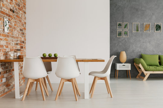 Wooden dining table and chairs by an exposed brick wall in a bright and natural living room interior of a modern loft