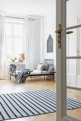 Door and carpet in white minimal bedroom interior with poster above bed next to window. Real photo