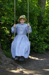 Girl dressed in vintage blue dress on tree swing