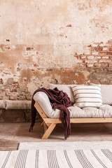 Red blanket and cushions on grey settee in living room interior with brick wall and carpet. Real...