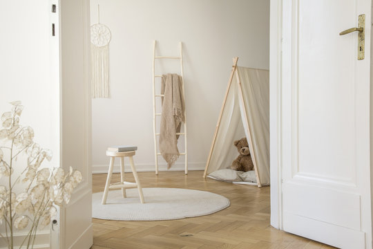 Real Photo Through The Door Of Kid Room Interior With Blanket On Ladder, Stool With Book, Play Tent With Teddy Bear And Herringbone Parquet