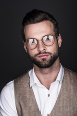 portrait of handsome confident man in glasses and stylish vest, isolated on grey