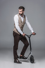 stylish elegant young man posing on modern scooter on grey