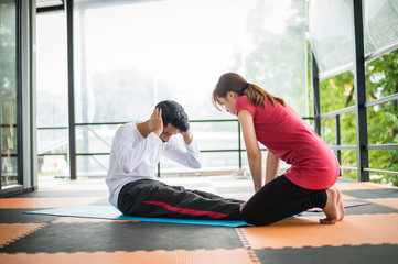 Fototapeta na wymiar woman trainer help sportsman sit ups in gym