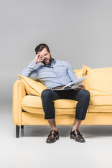 confused businessman with newspaper sitting on yellow sofa, on grey