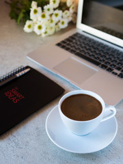 Workspace with cup of coffee, laptop, notebook and white flowers