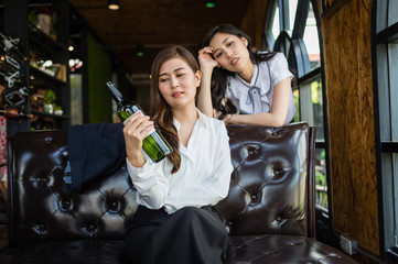 two business woman sitting in restaurant, and very drunk, her hand holding bottle of wine.