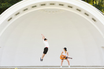 Woman playing guitar, man jumping next to her