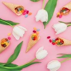 Beautiful pattern with bright sugar candy in waffle cones and white flowers on pink background. Flat lay, top view