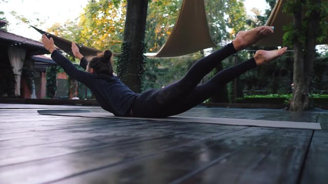 Girl doing Shalabhasana, locust pose. Young woman with oriental appearance practicing yoga alone on wooden deck in tropical island. Sport, fitness, healthy lifestyle concept.