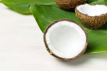 Ripe coconut and tropical leaves on a light wooden background, minimal flat lay style. Creative summer and food concept. Tropical fruit