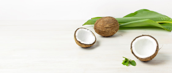 Ripe coconut and tropical leaves on a light wooden background, minimal flat lay style. Creative summer and food concept. Tropical fruit