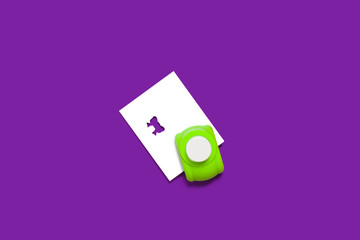 plastic green hole puncher with a sheet of paper in it standing on the purple background. concept...